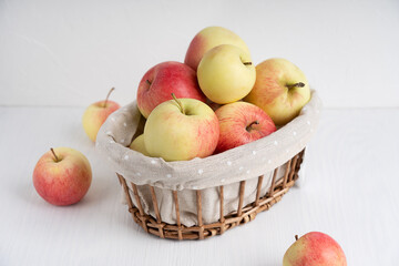 Group of organic tasty red and yellow apples in wicker basket on simple white wooden background at kitchen table showing healthy lifestyle and vegetarian dietary eating. Horizontal orientation image