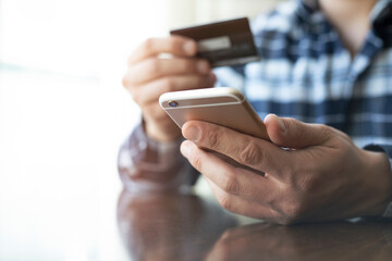 Man's hands holding a credit card and using a smart phone for online shopping