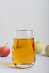 Organic transparent apple juice poured in drinking glass standing on white wooden background surrounded by raw ripe fruits showing healthy lifestyle and vegetarian eating. Vertical orientation image