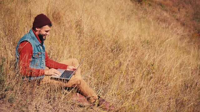 Side view of man talking on video call on laptop, sitting on hiil