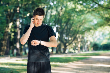 Fototapeta na wymiar Man in summer sports uniform running in the city park with smartwatch for measuring speed, distance and heart rate. Wireless earphones. Training outside