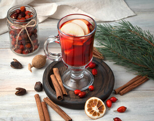 A glass of mulled wine with fruit, cinnamon and pine branches on a wooden background. Holiday...