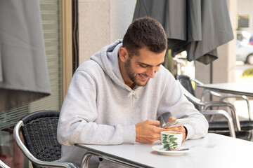 Fototapeta na wymiar young man on the terrace with mobile phone drinking coffee