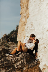 Young loving couple sitting and kissing on a stone against the background of white cliff.