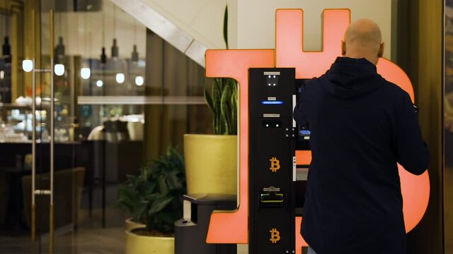 Bald man uses Bitcoin ATM machine in mall for cryptocurrency exchange