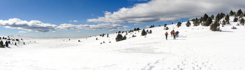 Panoramic of people walking in a snow landscape with snowshoes and backpacks in the Pyrenees. Hiking and skiing winter sport.