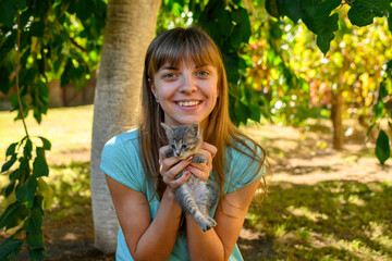 Beautiful woman in blue shirt holding little gray kitten in hands.
