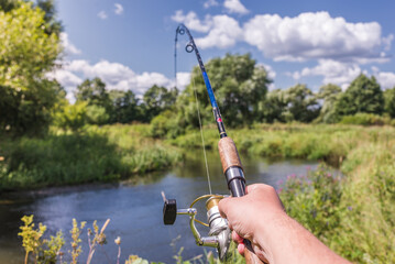 Male hand holding a fishing rod/Male hand holding a fishing rod from the first person. On a sunny day
