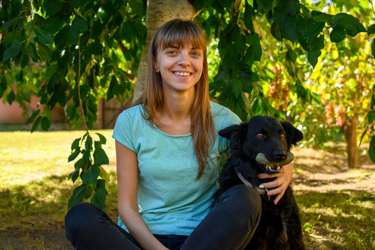 Young woman sitting in backyard on grass with beautiful black dog.