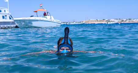 man in a full face snorkeling mask floats on the sea.
