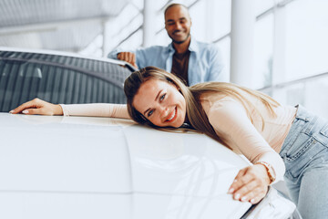 Young couple man and woman hugging their new car in a car shop