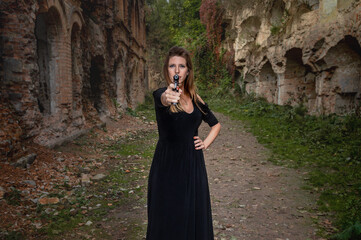 Young woman points a gun at the camera against the background of the ruins of the fortress