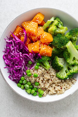 Vegetarian quinoa and broccoli lunch Buddha bowl with baked butternut squash or pumpkin, green peas and red cabbage, top down view