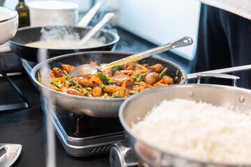 Poêle sur un réchaud en train de chauffer une recette de poulet asiatique et riz à côté