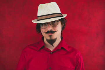 Young man with hat in red shirt on the red background. male portrait in eyeglasses