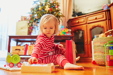 Adorable toddler girl in pajamas unpacking presents on Christmas morning
