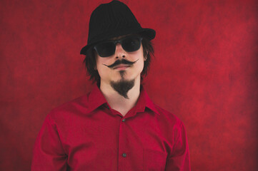 Young man with hat in red shirt on the red background. male portrait in sunglasses