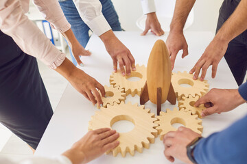 Hands of business people colleagues fixing wooden gears around wooden rocket in office