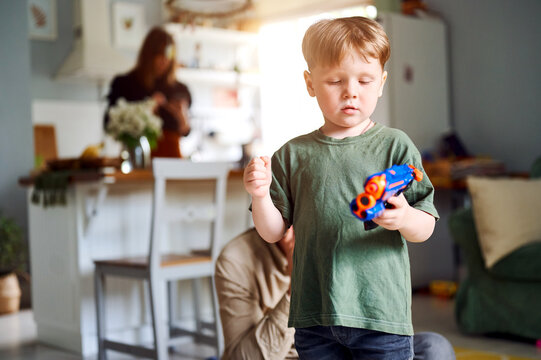 Young caucasian preschool boy playing with plasik toy, kid with colorful pistol or gun