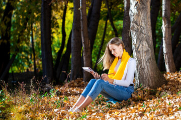 Young girl draws with a pencil in the sketchbook, autumn park outdoor