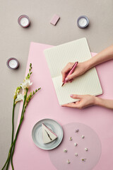 Obraz premium Minimal composition of female hands writing in blank planner over pink graphic background with floral decor, copy space