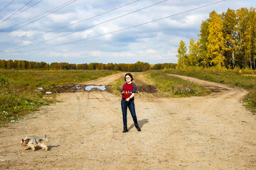 A girl walks her dog near the forest in autumn.