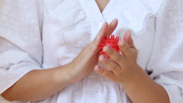 Close-up of a nervous girl's hands playing with an antistress toy in a shape of red virus ball with copy space
