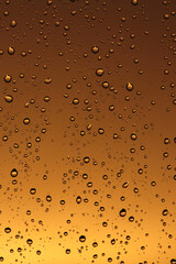 Rain drops on the window glass. Drops of water on window, yellow and orange sunset in background.