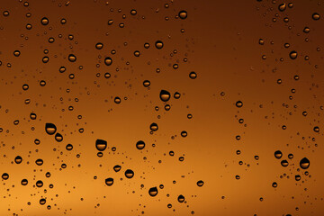Rain drops on the window glass. Drops of water on window, yellow and orange sunset in background.