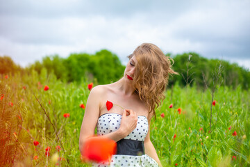 A young long-haired girl enjoys the colors of nature on a blooming poppy field on a hot summer day