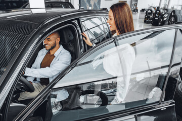 Young attractive woman salesperson in car showroom showing a car to her male client