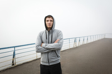 Man in gray hoodie stay on bridge in foggy morning