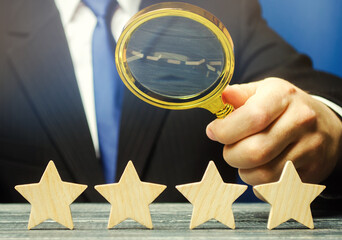 A man holds a magnifying glass over four stars. The evaluation of visitors. Quality level, good service. Best customer rating. Feedback. Rating of hotels and restaurants. Selective focus