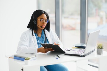 African doctor wear headset consult patient make online webcam video call on laptop screen. Telemedicine videoconference remote computer app virtual meeting. Over shoulder videocall view.