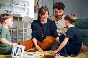 Young caucasian parents spending time at home with sons and reading books on the floor. Happy family playing with preshool children. Home education concept