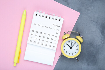 Fototapeta na wymiar Calendar page with alarm clock and pen on grey background