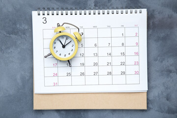Fototapeta na wymiar Calendar page with yellow alarm clock on grey background