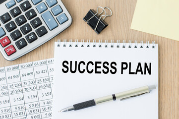 text SUCCESS PLAN on a notebook next to which is a pen, a calculator on the table. Business and finance concept