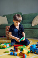 Fototapeta premium Preschool caucasian boy playing with constructor sitting on the floor, lots of colorful plastic blocks constructor
