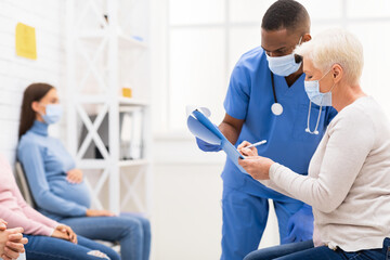 Fototapeta premium Mature Patient Lady Signing Papers With Doctor In Hospital Waiting-Room