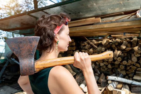Young adult beautiful happy attractive caucasian brunette woman portrait have fun enjoy holding old rusty axe chopping firewood at wood store on backyard. Female person vintage retro pinup style