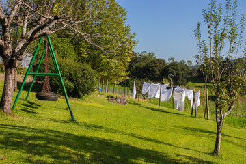 White linen on clothesline and baby swing in garden. White bedsheets on fresh air in the village. Housework concept. Outdoor laundry. Backyard on idyllic sunny day. Homework concept. 