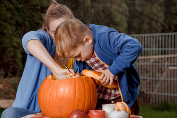 A boy and his mother cut a pumpkin. A young mother and son are preparing a pumpkin for Halloween. Preparing for Halloween. Peel an orange pumpkin.