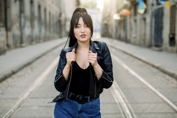 Beautiful young Asian mixed raced woman model, wearing stylish casual black leather jacket and jeans, standing on the tram road and enjoying the walk in the city
