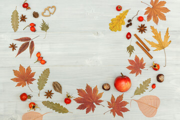 Autumn pattern frame of dried leaves, rosehip berries, anise, cinnamon and two small wooden hearts. Top view On a light wooden background, with space.