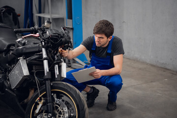 Fototapeta na wymiar A mechanic inspects a motorcycle. He is wearing a blue overalls