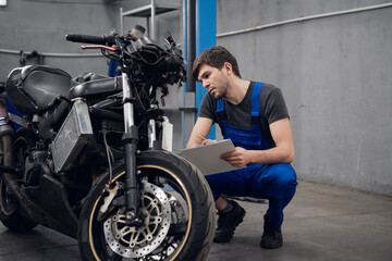 Obraz na płótnie Canvas Mechanic in uniform writes on a clipboard and checks a motorcycle