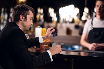 a man holds a plastic card, pays for a cocktail in a bar.