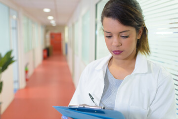 female nurse making notes on clipboard in hospital corridor