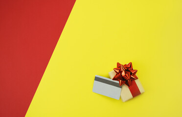 Gift box with a red ribbon and credit card on yellow-red background. Online shopping in quarantine. Christmas and New Years sale. Choosing and buying gifts. Selective focus. Flat-lay. Copy space